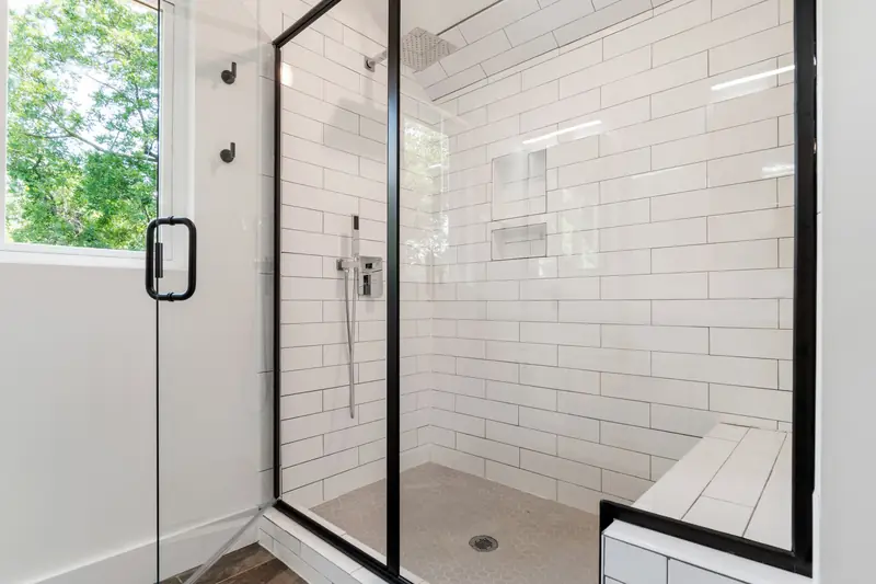Newly plumbed walk-in shower with white tiles and black fittings